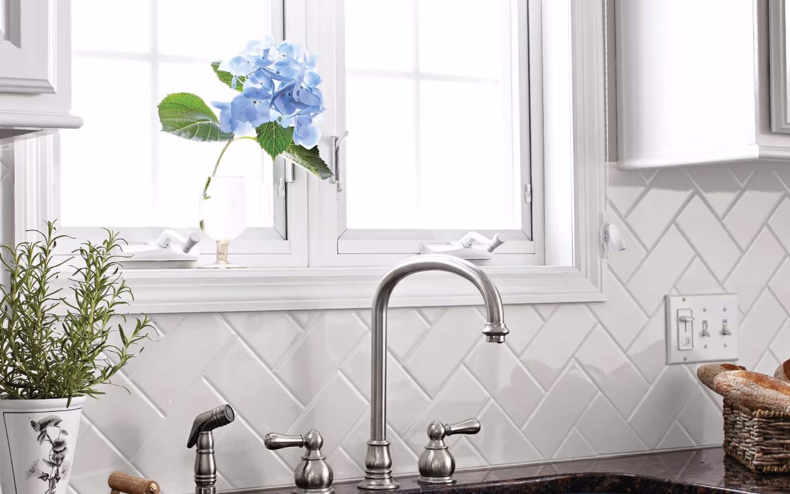 White herringbone tile kitchen backsplash behind sink and stainless faucet