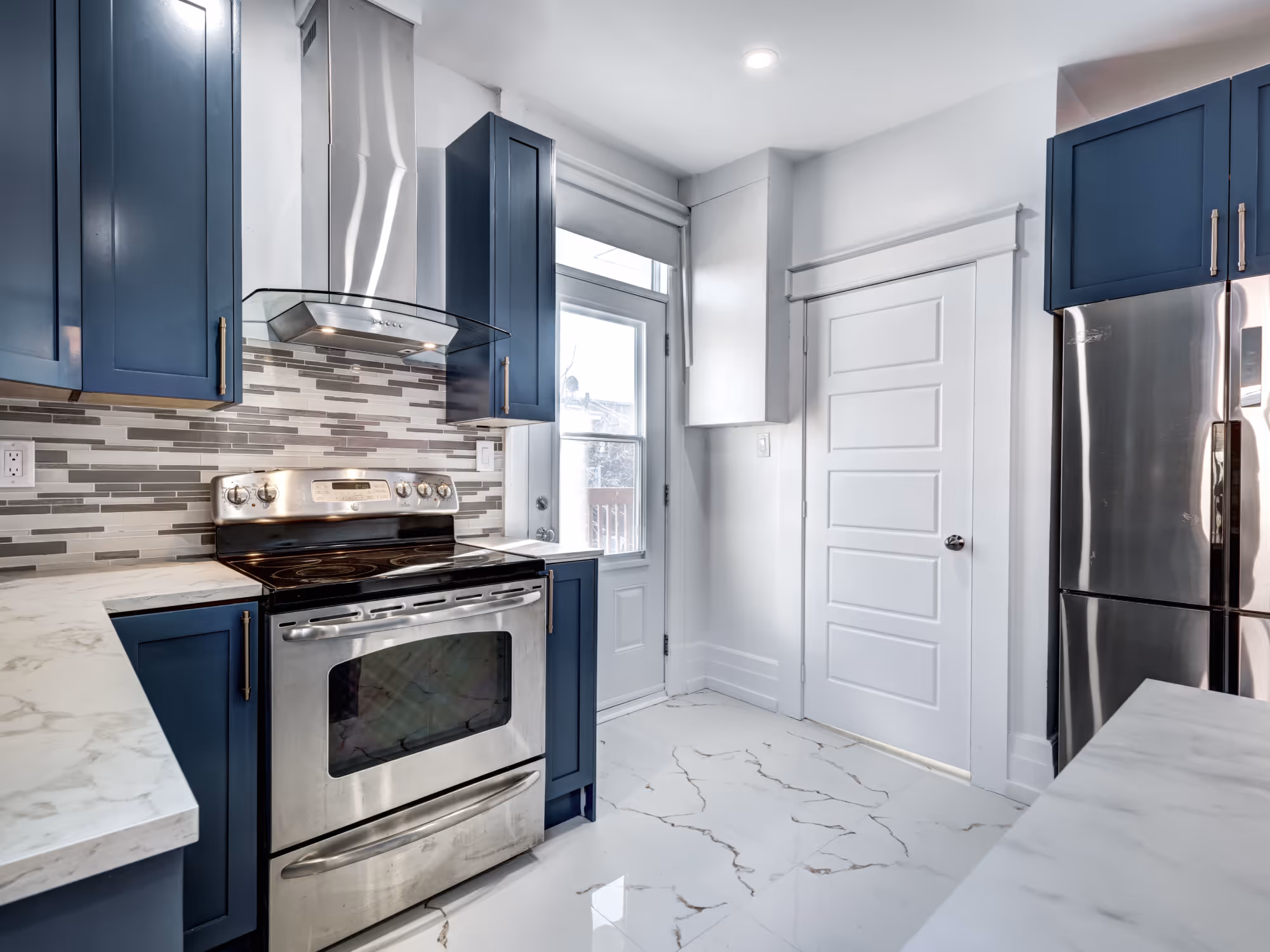 Kitchen with marble-look tile flooring, navy cabinets, and stainless appliances