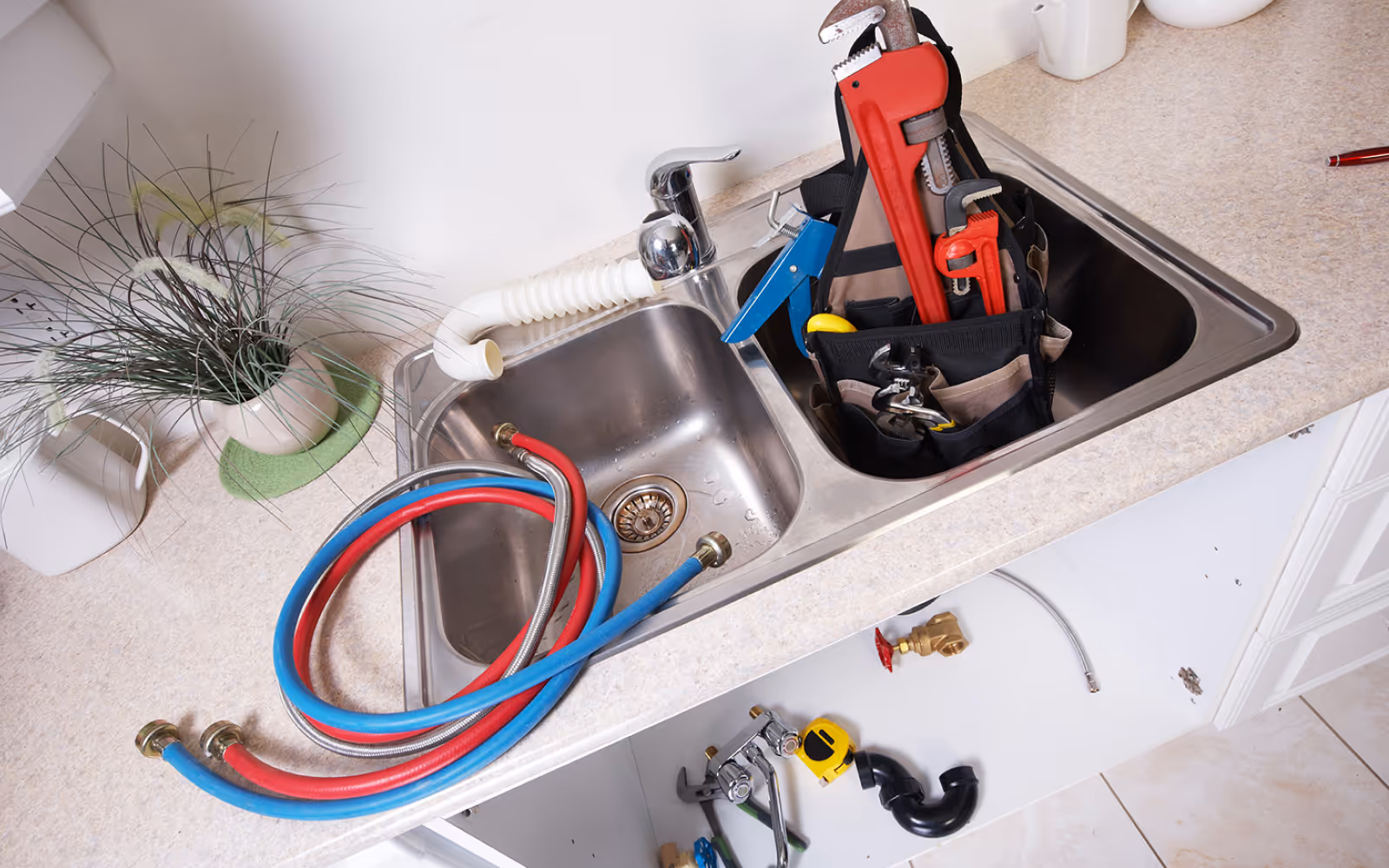 Kitchen sink plumbing repair with tools, supply lines, and drain parts