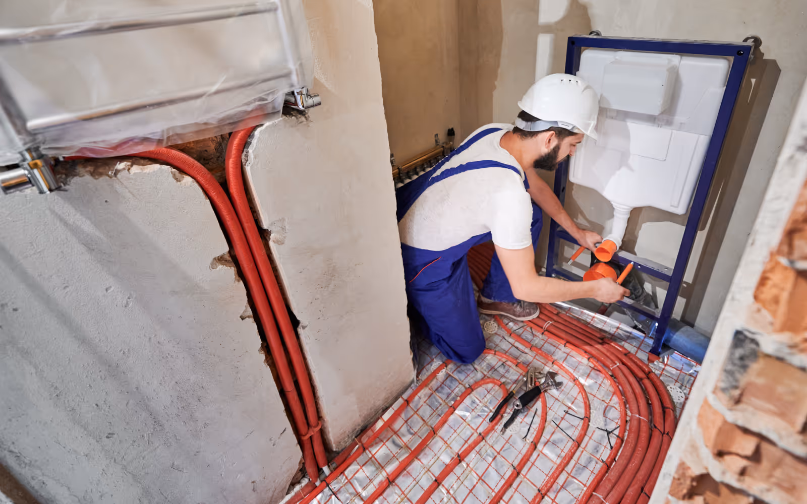 Plumbing rough-in work in progress with in-wall toilet frame and radiant floor tubing installation