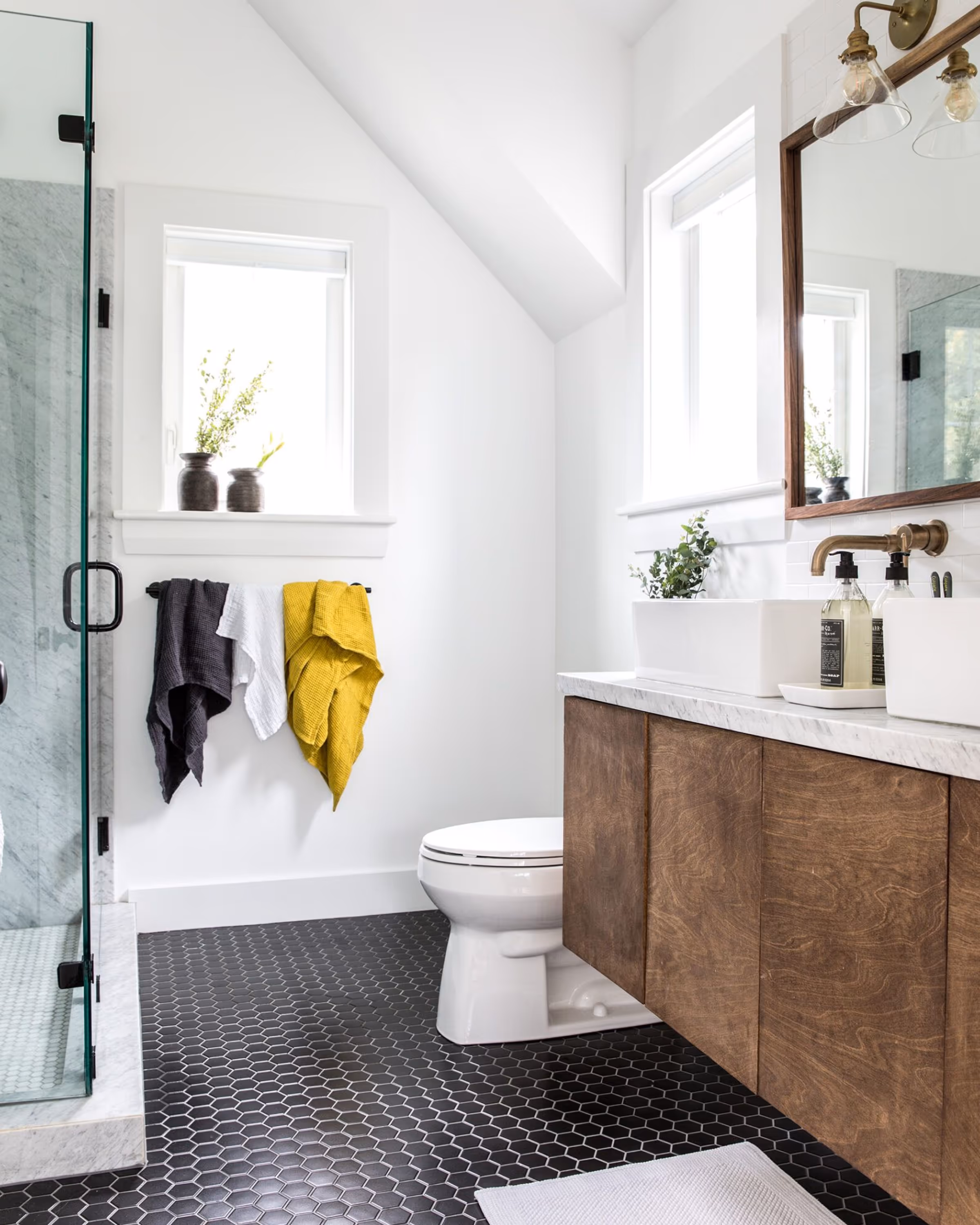 Bathroom renovation with wood vanity, brass faucet, glass shower, and hex tile flooring