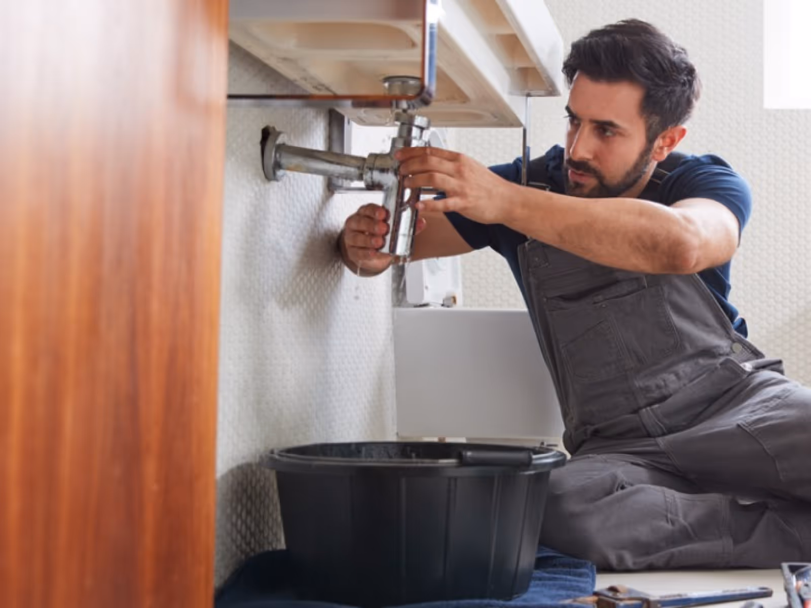 Handyman repairing under-sink plumbing and drain connection in Durham Region